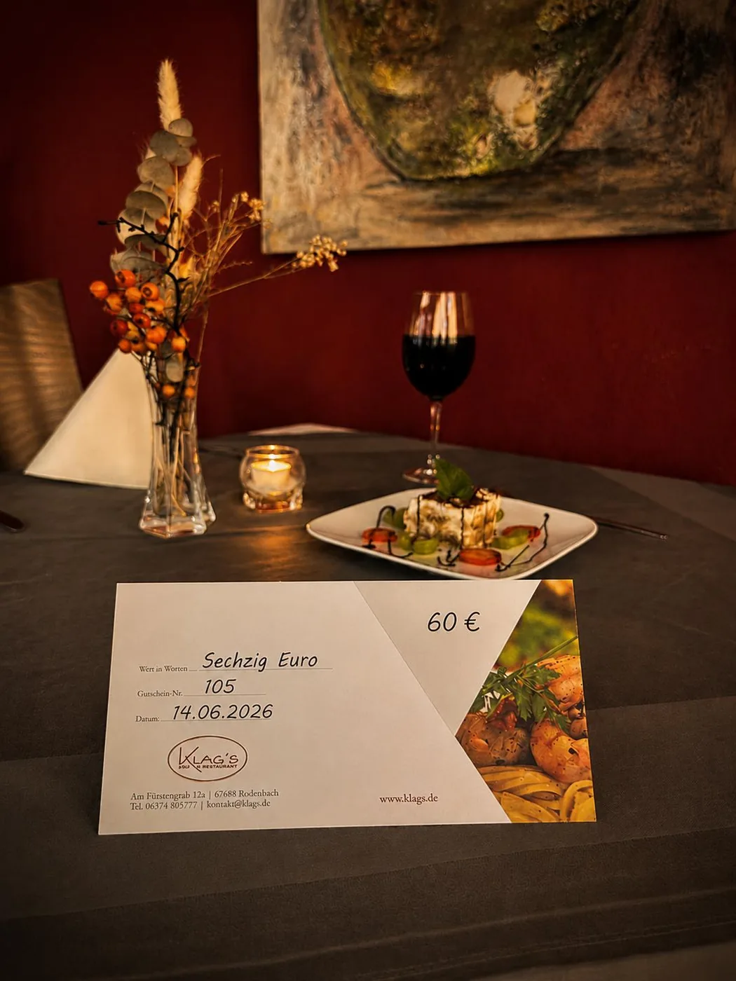 Klag's Restaurant gift voucher for 60 € on table with candlelight, red wine, tiramisu and dried flowers